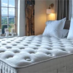Luxurious, tufted mattress with white pillows in a cozy bedroom, featuring large windows with scenic countryside views and natural light.