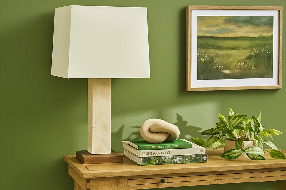 green wall featuring a lamp, a potted plant, and a framed painting, creating a cozy interior atmosphere.